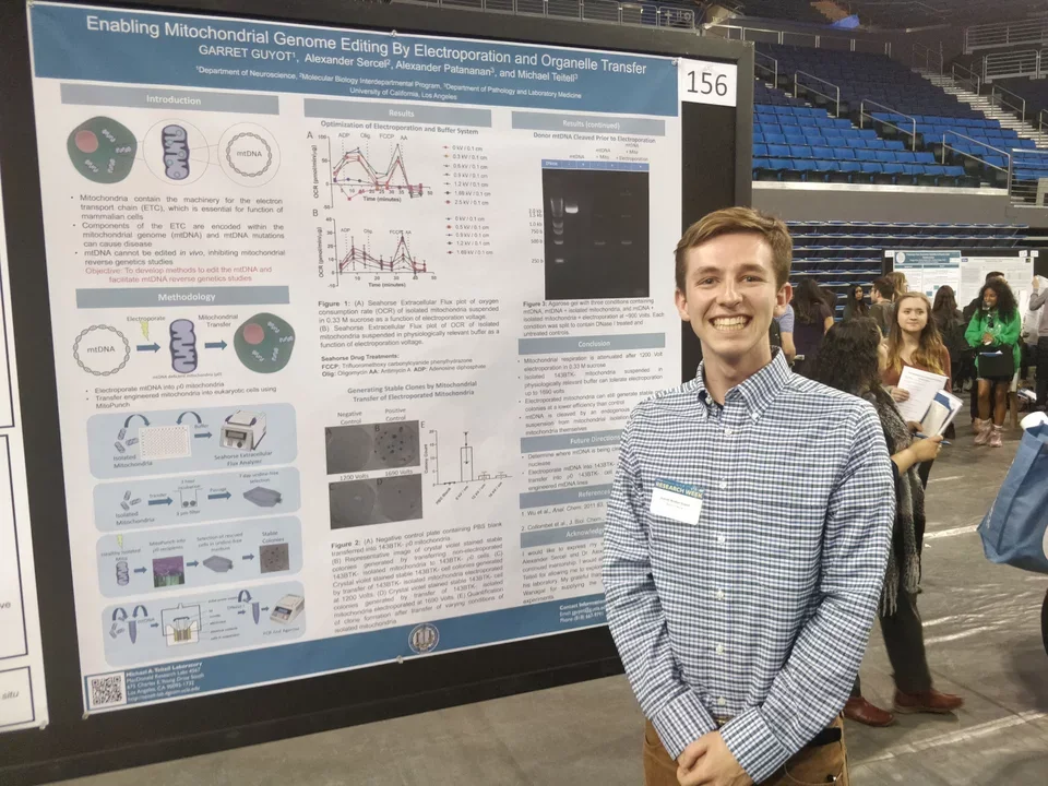 A smiling undergrad student stands in front of his poster presentation