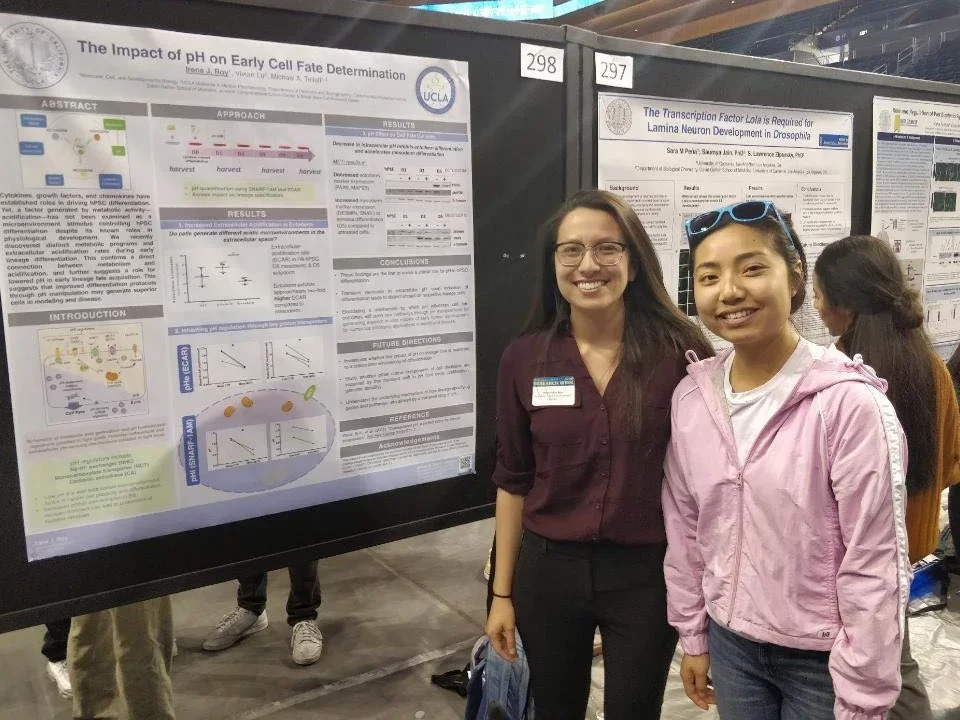 Two students stand smiling in front of a poster presentation
