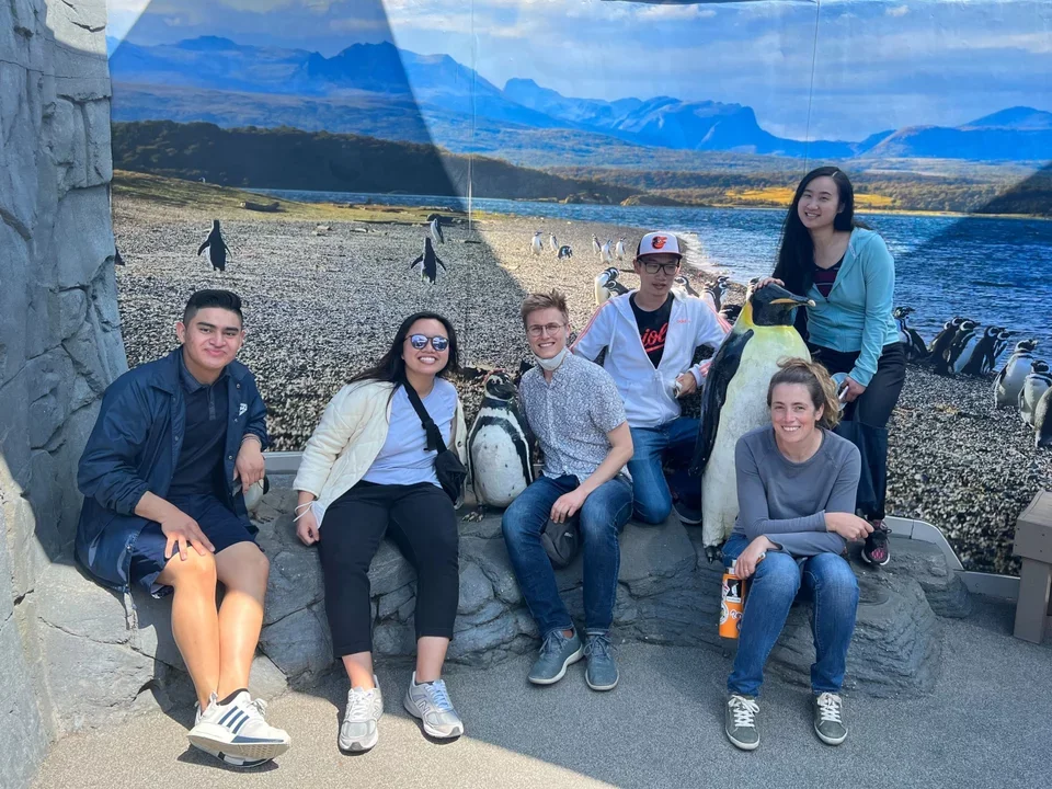 Lab members sit smiling next to statues of penguins at the Long Beach Aquarium