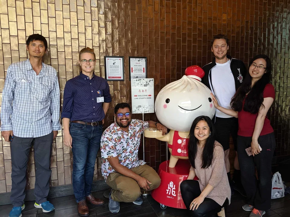 Teitell lab members pose smiling next to a dumpling mascot outside of Din Tai Fung