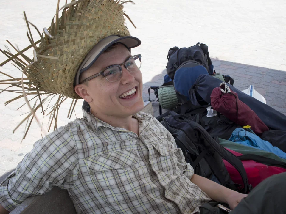 Teitell lab manager Alex Napior sits smiling in a straw hat amongst heaps of luggage