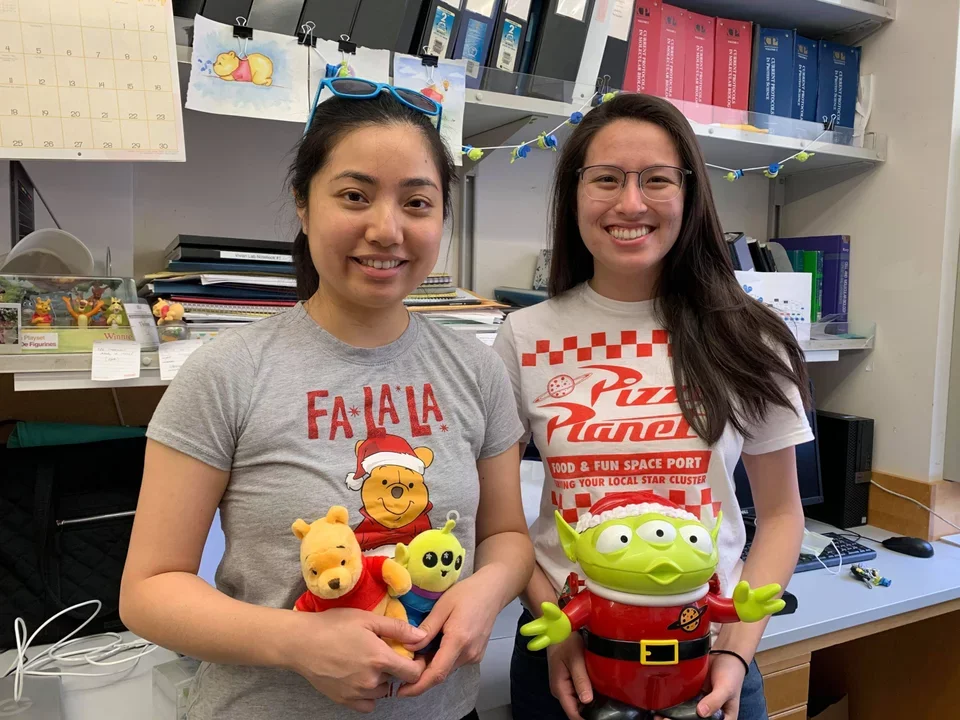 Two lab members hold stuffed toys in lab - a pooh bear and alien from the movie Toy Story