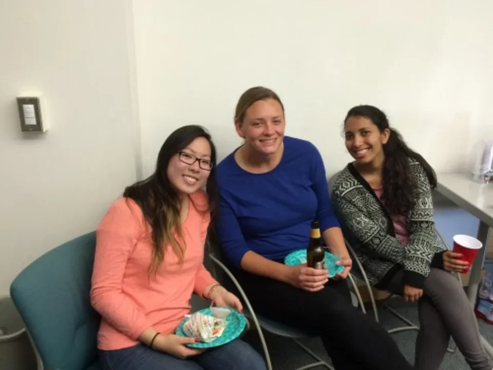 Three lab members sit smiling with plates of cake 