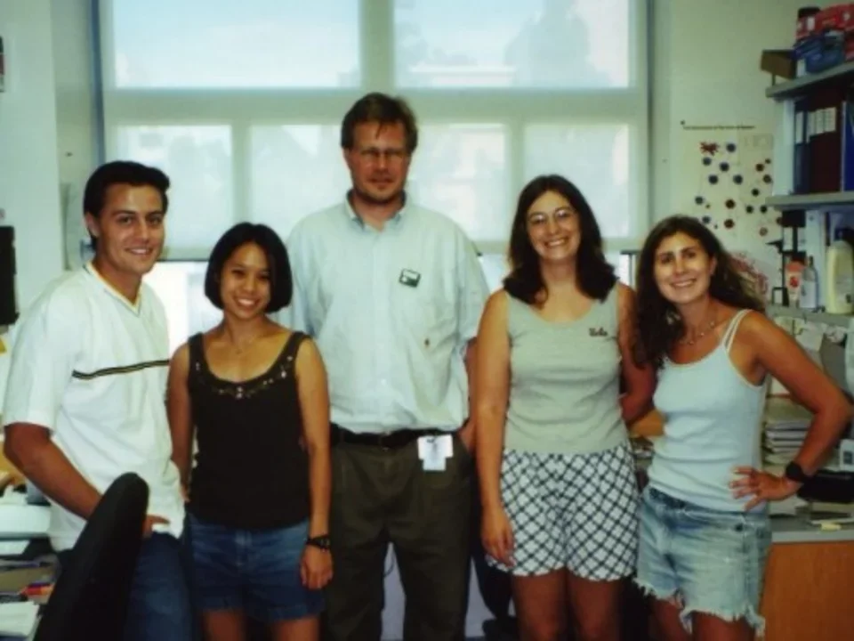 A photo from 2001 of five lab members standing in a line in the lab and smiling