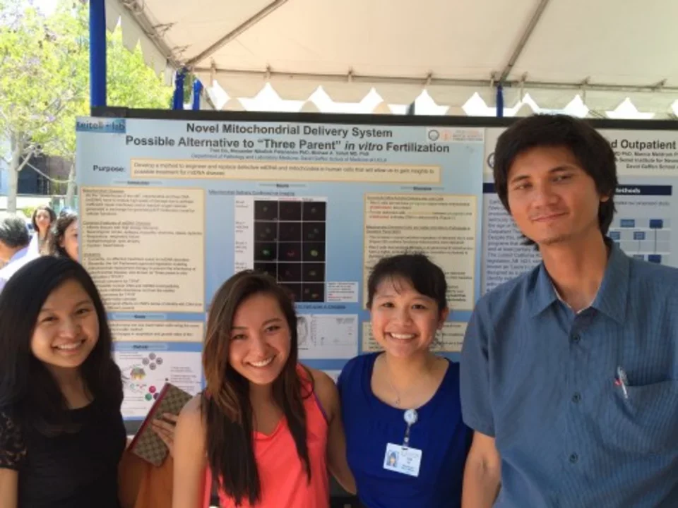 Photo from 2015, four lab members stand smiling in front of Tran's poster presentation