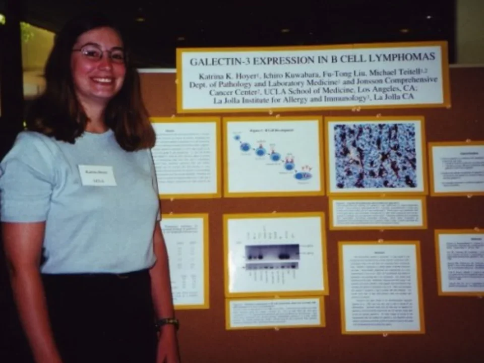 A Teitell lab member stands smiling in front of her research poster