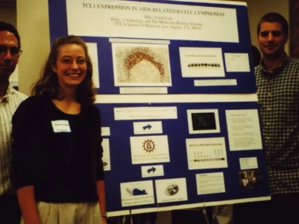 a photo taken in 1999 of a Teitell Lab member standing next to her research poster. She is smiling. 